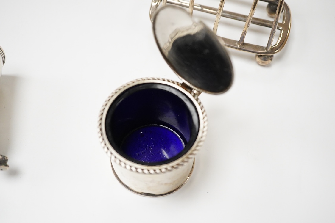 An Edwardian silver mug, on claw and hoof feet, William Hutton & Sons, London 1909, height 83mm, together with a silver butter shell, mustard pot and a silver five bar toastrack, 17oz.
